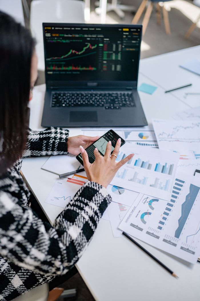 services-02 Businesswoman evaluating stock market trends using graphs and smartphone in office.